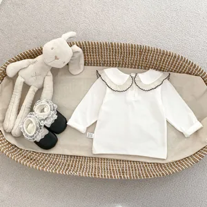 Detail von weißem Langarm-Babytop mit Rüschenkragen und schwarzen Spitzen-Schuhen