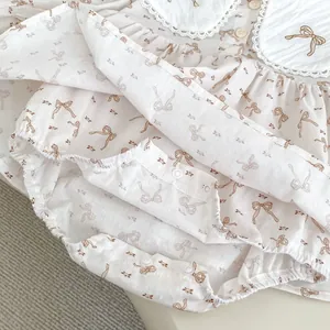 Détail du body bébé avec col en dentelle, broderie de nœuds et tissu en coton fleuri