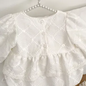 Close-up of baby romper showing delicate flower embroidery and lace hem on white cotton
