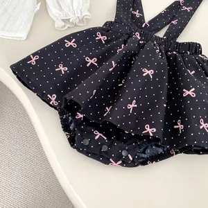 Gros plan d'un body à bretelles pour bébé à pois noirs et nœuds roses avec pressions