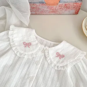 Détail de chemise bébé fille avec col poupée en dentelle et broderie nœud rose