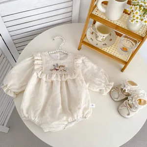 Macro detail of cream baby bodysuit with flower embroidery and ruffled lace collar