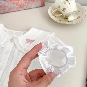Détail de chemise bébé blanche avec broderie nœud rose sur col à volants et poignets