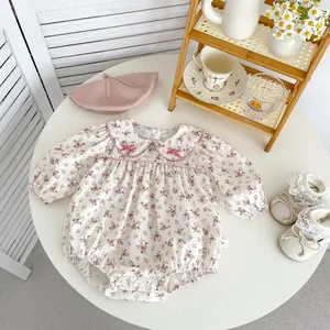 Floral baby bodysuit with Peter Pan collar and bow details on white wooden tabletop