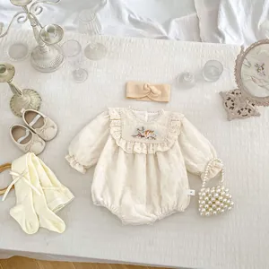 Close-up of floral embroidery and delicate lace trim on ivory cotton baby bodysuit