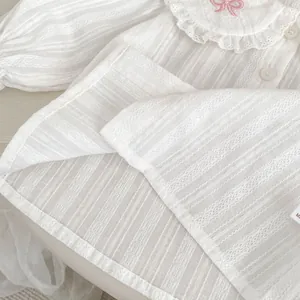 Détail de la blouse blanche pour bébé avec col à volants et broderie nœud rose