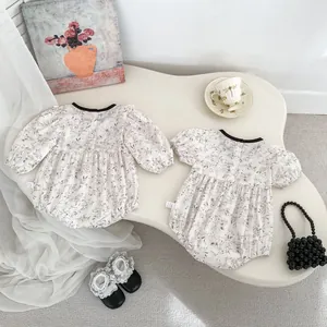 Detailed view of floral baby rompers with back buttons and snap bottom on a white desk