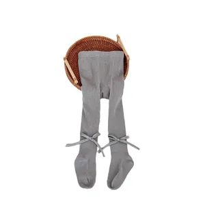 Grey rib-knit baby footed tights with sweet bow details on a woven tray display