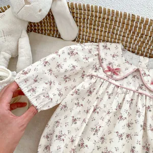 Detail of baby floral bodysuit with pink bow and peter pan collar on cream fabric