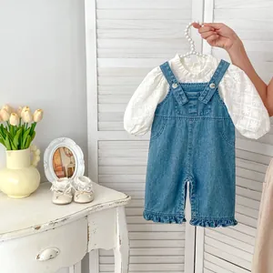 Détail du haut blanc brodé et de la barboteuse en jean avec volants pour bébé fille