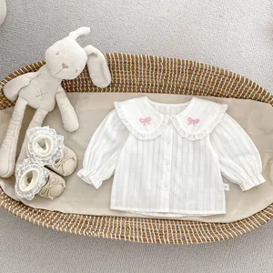 Détail d'une chemise bébé en coton blanc avec col en dentelle et broderie nœud rose