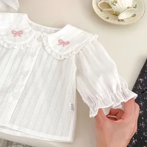 Detalle de camisa blanca de manga larga con cuello de encaje y bordado de lazo rosa