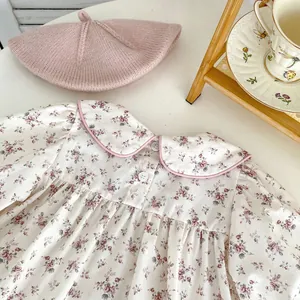 Detail of floral baby bodysuit with Peter Pan collar and pink knit beret on a tray