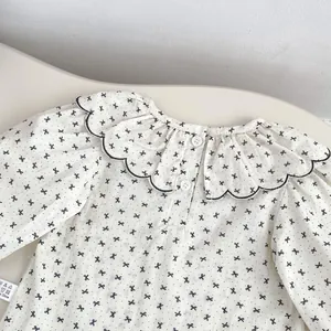 Détail d'un t-shirt bébé manches longues en coton avec col festonné et nœuds noirs