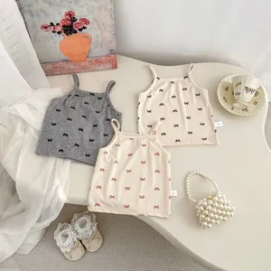 Three toddler cotton rib camisoles with bow patterns on a minimalist cream background