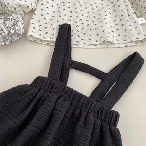 Détail de l'ensemble bébé montrant la barboteuse noire texturée et la chemise blanche