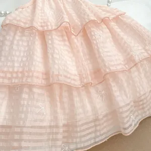 Makroaufnahme von rosa gestuftem Kleid mit zarten weißen Schleifenstickerei-Details