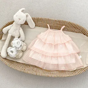Detailaufnahme von hellrosa gestuftem Babykleid mit gestickten Schleifen in einem Korb