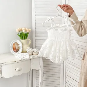 Détail de la barboteuse en dentelle blanche pour bébé avec volants et bretelles à nœuds