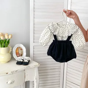 Détail d'une chemise bébé à col volanté et d'un short à bretelles en velours noir