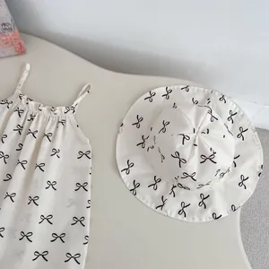 Detail of infant summer romper set featuring black bow print and matching sun hat on beige
