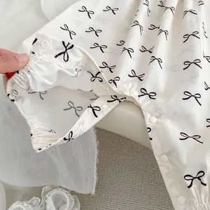 White baby bodysuit with bow prints and snap buttons, shown with matching hat