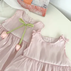 Flat lay of pale pink sleeveless baby dress with tulip accent and satin finish