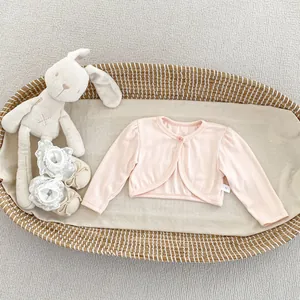 Detail of light pink knitted baby cardigan with a single button in a cozy nursery setting
