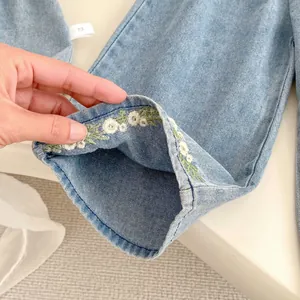 Detailed view of baby denim pants featuring delicate white flower embroidery and size 73 tag