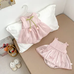 Detailed view of pink silk baby romper dress with green bow and tulip charm on a hanger