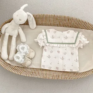 Detalle de camisa de bebé floral con cuello marinero y volantes en cesta de mimbre