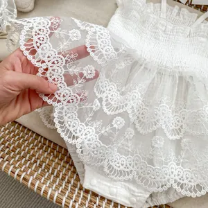 Détails de broderie sur une barboteuse en dentelle blanche pour bébé avec motifs floraux