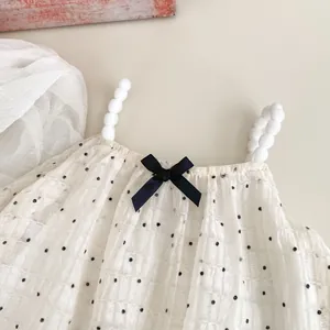 Detail of white polka dot baby top featuring pom-pom straps and a black satin bow accent