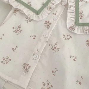 Detalle de camisa floral para bebé con cuello de volantes, cinta verde y textura de botones