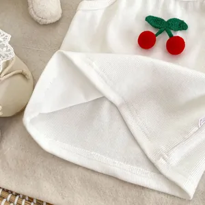 Detail of white ribbed cotton baby vest with 3D plush cherry applique and soft texture