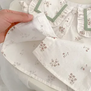Detalle de blusa floral para bebé con cuello de muñeca con volantes y botones blancos