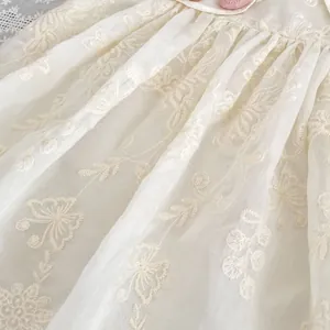 Detailed close-up of floral embroidery on ivory dress with a pink satin rose