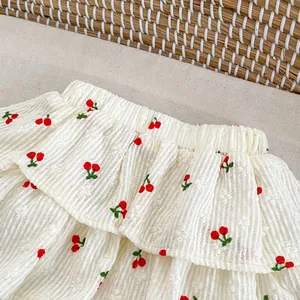 Detailed view of white cotton skirt with cherry embroidery and layered ruffle texture