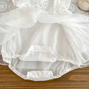 Close-up of baby romper dress showing bottom snap buttons and floral lace embroidery