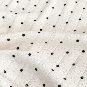 Nahaufnahme des weißen Rippstrickstoffs mit schwarzen Punkten und feinen Nahtdetails