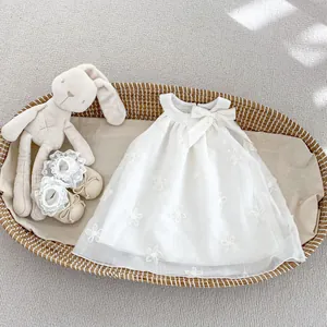 Dettaglio dell'abito da bambina in tulle bianco con ricami floreali e scarpine in pizzo abbinate