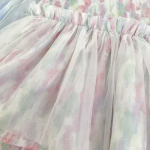 Détail d'un body bébé à fleurs avec tulle blanc superposé et taille élastique à volants