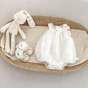 Detail of white infant romper with floral embroidery and bow in a woven basket