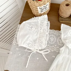 Close-up of white baby bonnet with floral embroidery and lace ruffles on wooden desk
