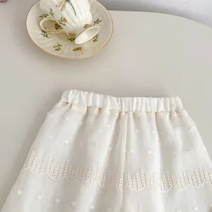 Detail of white Swiss dot fabric with delicate lace embroidery and scalloped hemline