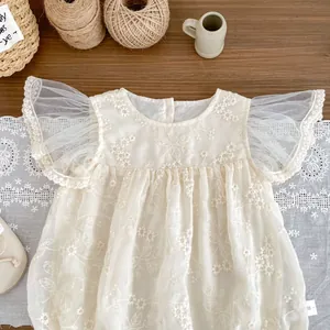 Detail of baby lace romper with floral embroidery and mesh flutter sleeves on wood
