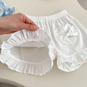 Detail of white cotton baby shorts with elastic waist, heart pocket and ruffle hem