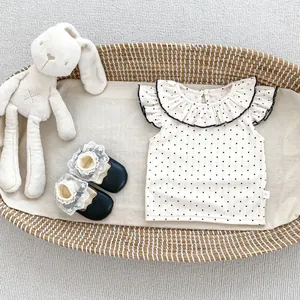 Detail von gepunktetem Top mit Rüschenkragen und Babyschuhen mit Spitze im Korb