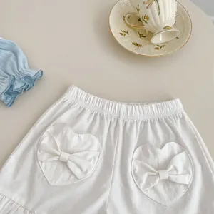 Detail of white cotton girl shorts featuring heart pockets with bow accents and ruffled hem