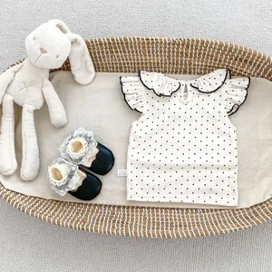 Detailaufnahme von Baby-Oberteil mit Punkten, Rüschenkragen und schwarzen Schleifenschuhen